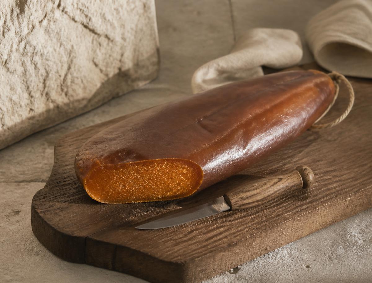 A large wax-coated whole bottarga lobe beside a smaller vacuum-packed lobe on a pale linen cloth